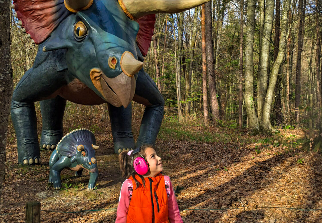 Kép egy álmodozó gyermek csendes napjairól zajszűrő fejhallgatóval a Triceratops mellett a Styrassic Parkban