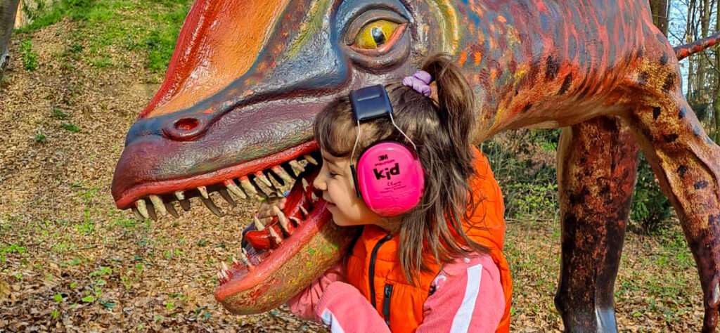 Bild an Stillen Tagen von Kind mit Lärmschutzkopfhöhrer, welches mit Dino kuschelt